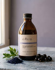 Evera Shampoo No 5 Brunette with indigo powder and boxwood sprig on grey travertine, dusty lavender backdrop